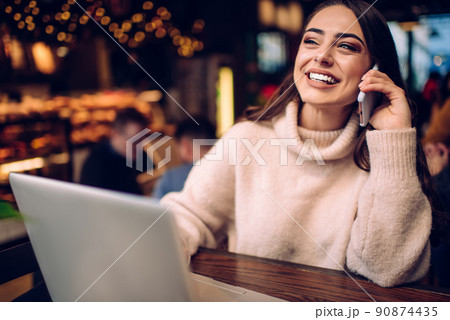 Happy businesswoman talking on smartphone in front of laptop in modern restaurant 90874435