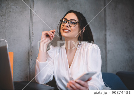 Positive young woman using mobile while having break in cafe Positive young woman using mobile while having break in cafe 90874481