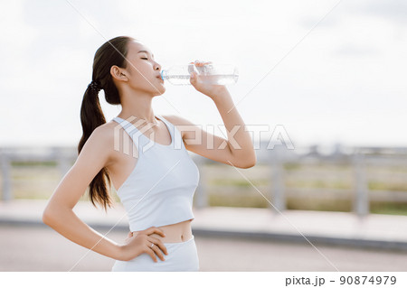Beautiful Asian women in sportswear standing outdoors holding water bottle for drink after exercise. Healthy women concept. Running workout. Beautiful Asian women in sportswear standing outdoors holding water bottle for drink after exercise. Healthy women concept. Running workout. 90874979