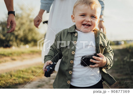 Funny Toddler Boy Holding Toys in Hands and Running Away from His Parents Outdoors Funny Toddler Boy Holding Toys in Hands and Running Away from His Parents Outdoors 90877369