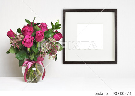 Bouquet of pink rose flowers in a glass vase on table and brown empty frames on white wall Bouquet of pink rose flowers in a glass vase on table and brown empty frames on white wall 90880274
