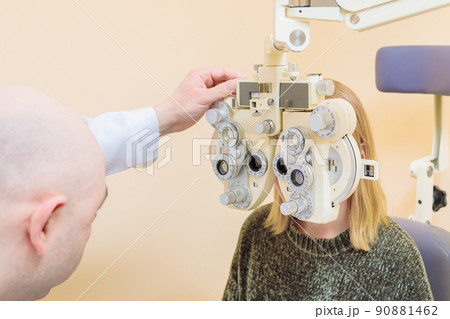 A male ophthalmologist checks a girl's eyesight using a phoropter. Vision treatment A male ophthalmologist checks a girl's eyesight using a phoropter. Vision treatment 90881462