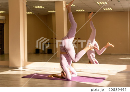 Young sporty woman, fitness instructor in pink sportswear doing stretching and pilates on yoga mat in the studio with mirror. Female fitness yoga routine concept. Healthy lifestyle and harmony. 90889445