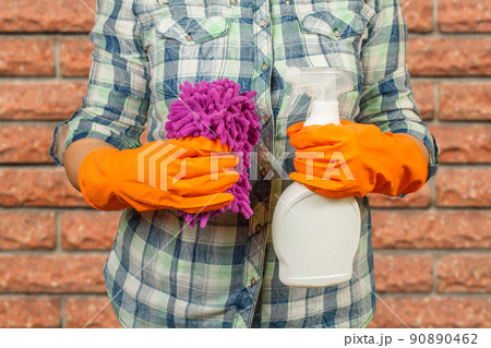 Women's hands in protective gloves with the bottle of washing liquid and the rag. Women's hands in protective gloves with the bottle of washing liquid and the rag. 90890462
