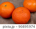 Three tangerines on a table covered with a homespun cloth with a rough texture 90895974