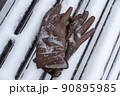 Brown leather gloves forgotten on a snow-covered bench in a winter park 90895985
