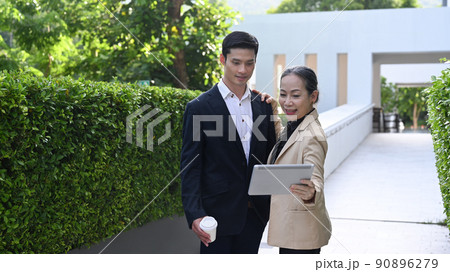 Attractive mature businesswoman with business partner discussing information on digital tablet together while standing at modern office district 90896279