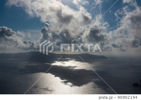 ギリシャ　サントリーニ島のフィラから見える太陽に雲がかかって影の出来たエーゲ海とティラシア島 90902194