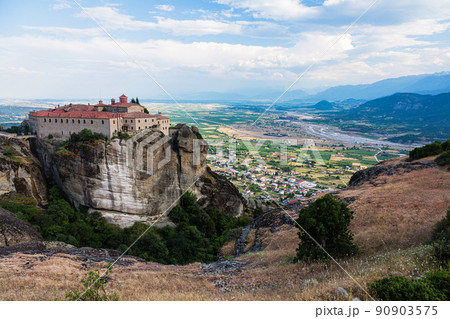 ギリシャ　メテオラの断崖絶壁の岩山の上に建つ聖ステファノス修道院と奇岩群の隙間から覗くカランバカの街 90903575