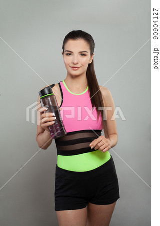 Smiling active woman holding water bottle or protein shake on grey background 90904127