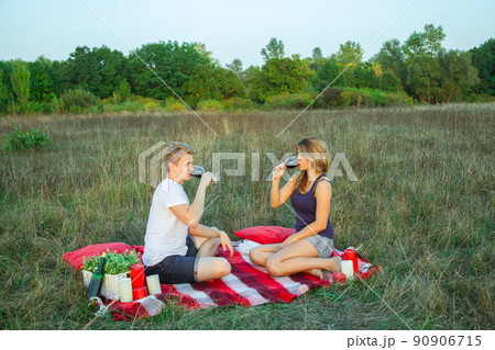 Beautiful young happy loving couple on picnic lying down on plaid in field on sunny summer day enjoying, holding and drinking wine and resting. looking at camera and smiling. Beautiful young happy loving couple on picnic lying down on plaid in field on sunny summer day enjoying, holding and drinking wine and resting. looking at camera and smiling. 90906715