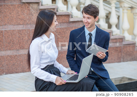 Boss in blue suit and his assistant in white blouse and black skirt discussing their work outdoors. Boss in blue suit and his assistant in white blouse and black skirt discussing their work outdoors. 90908265