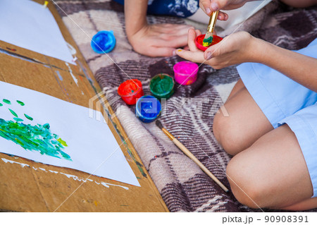 Older sister trying to teach her brother to paint and posing in the park on summer time, looking at camera and smiling. 90908391