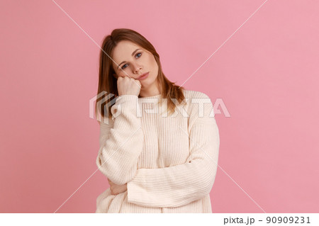 Portrait of blond woman leaning on hand and expressing disinterest apathy with dull look, feeling lazy indifferent, wearing white sweater. Indoor studio shot isolated on pink background. Portrait of blond woman leaning on hand and expressing disinterest apathy with dull look, feeling lazy indifferent, wearing white sweater. Indoor studio shot isolated on pink background. 90909231