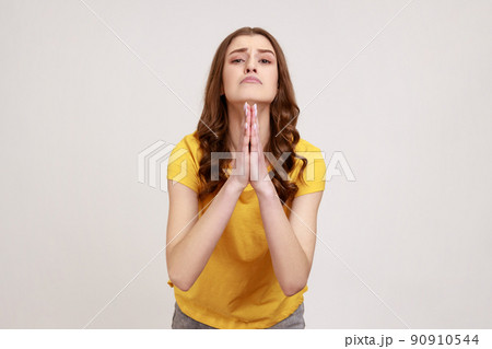 Please, I'm begging forgive. Adorable upset worried woman of young age with wavy hair looking with imploring desperate grimace, praying for help. Indoor studio shot isolated on gray background. Please, I'm begging forgive. Adorable upset worried woman of young age with wavy hair looking with imploring desperate grimace, praying for help. Indoor studio shot isolated on gray background. 90910544