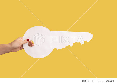 Closeup side view of woman hand holding big white house key, real estate advertisement, house purchase, apartment rent. Indoor studio shot isolated on yellow background. 90910604