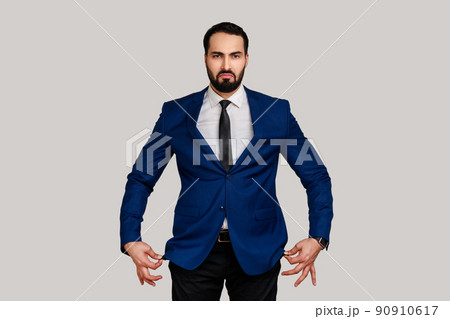 Portrait of sad unhappy bearded man showing empty pockets inside out, going bankrupt, no cash for living, wearing official style suit. Indoor studio shot isolated on gray background. Portrait of sad unhappy bearded man showing empty pockets inside out, going bankrupt, no cash for living, wearing official style suit. Indoor studio shot isolated on gray background. 90910617