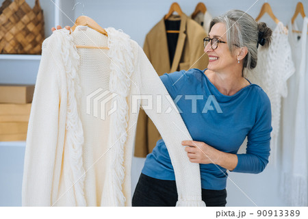 Elderly woman during chooses white sweater at home Elderly woman during chooses white sweater at home 90913389