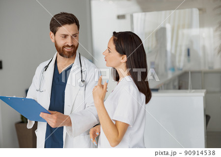 Doctor and nurse solve work issues standing near reception in clinic Doctor and nurse solve work issues standing near reception in clinic 90914538