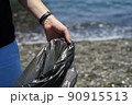 man hand collects garbage on the beach, holds garbage bag 90915513