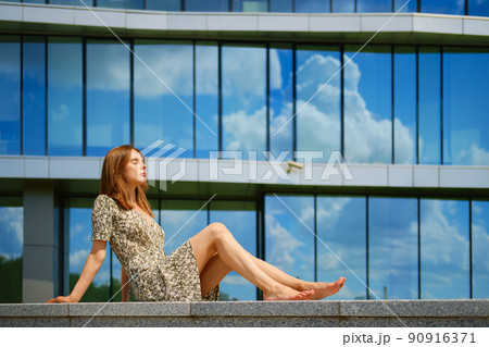 Barefoot woman in dress and sandals sitting in profile 90916371