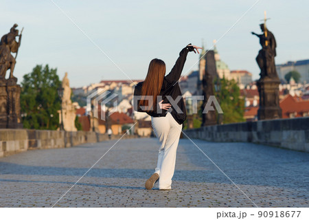 Young woman in casual stylish clothes dancing on the stone bridge of old town in a Prague. Active lifestyle and dancing concept. Young woman in casual stylish clothes dancing on the stone bridge of old town in a Prague. Active lifestyle and dancing concept. 90918677