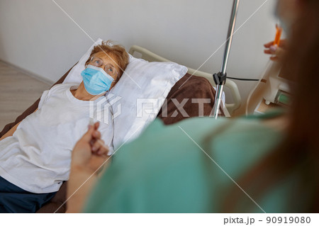 Nurse putting a drip in the arm of her patient in mask in modern medical clinic 90919080