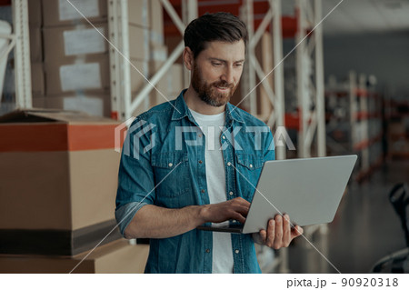 Handsome business owner working on laptop stands on own warehouse  90920318