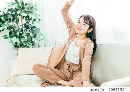 ソファでストレッチする女性（柔軟体操・腕・肩） 90925594
