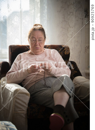 An old woman in beige sweater sitting in the armchair and knitting An old woman in beige sweater sitting in the armchair and knitting 90925769