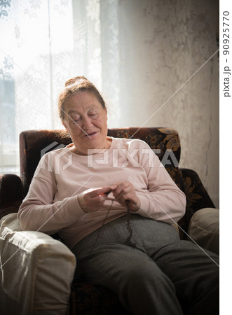 An old smiling woman sitting in the armchair and knitting 90925770