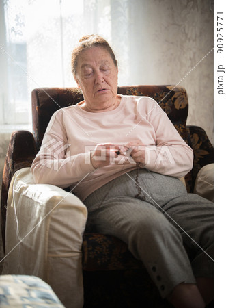 An old woman in sweater sitting in the armchair and knitting An old woman in sweater sitting in the armchair and knitting 90925771