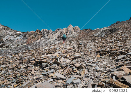 Solo trekking in the mountains. Man with a large backpack is climbing heavily on loose rock trail. Adventure solo traveling lifestyle concept, active weekend vacations on the wild nature. Solo trekking in the mountains. Man with a large backpack is climbing heavily on loose rock trail. Adventure solo traveling lifestyle concept, active weekend vacations on the wild nature. 90928321