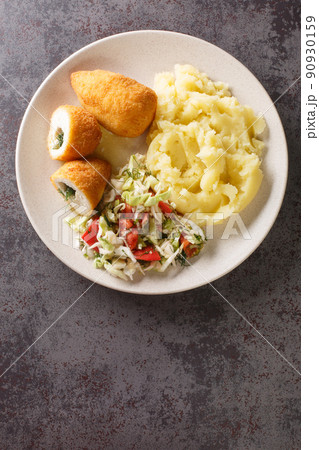 Ukrainian food Kyiv cutlet of chicken fillet with butter and herbs served with mashed potatoes and vegetable salad close-up in a plate. Vertical top view 90930159