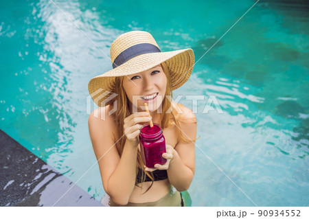Young woman drinking Dragon fruit smoothies on the background of the pool. Fruit smoothie - healthy eating concept. Close up of detox smoothie with Dragon fruit Young woman drinking Dragon fruit smoothies on the background of the pool. Fruit smoothie - healthy eating concept. Close up of detox smoothie with Dragon fruit 90934552
