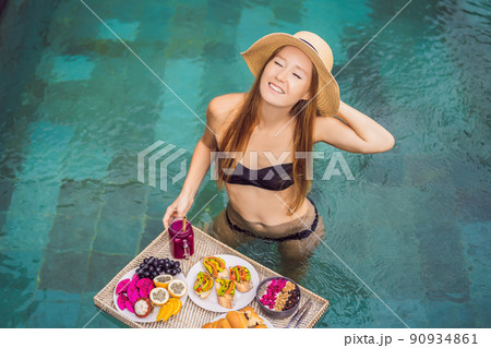 Breakfast tray in swimming pool, floating breakfast in luxury hotel. Girl relaxing in the pool drinking smoothies and eating fruit plate, smoothie bowl by the hotel pool. Exotic summer diet. Tropical Breakfast tray in swimming pool, floating breakfast in luxury hotel. Girl relaxing in the pool drinking smoothies and eating fruit plate, smoothie bowl by the hotel pool. Exotic summer diet. Tropical 90934861