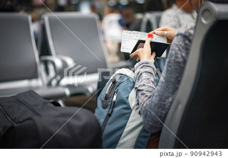 The woman checks her passport and plane ticket in the hand and waiting the plane in an international airport, Thailand. The woman checks her passport and plane ticket in the hand and waiting the plane in an international airport, Thailand. 90942943