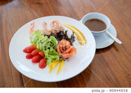 Salad raw salmon arranged to rose shape and boiled shrimp beside in the white dish on wood table. 90944058