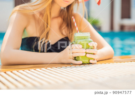 Woman with a green smoothies of spinach and banana on the background of the pool. Healthy food, healthy smoothies Woman with a green smoothies of spinach and banana on the background of the pool. Healthy food, healthy smoothies 90947577