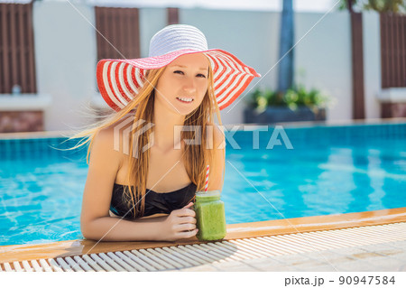 Woman with a green smoothies of spinach and banana on the background of the pool. Healthy food, healthy smoothies 90947584
