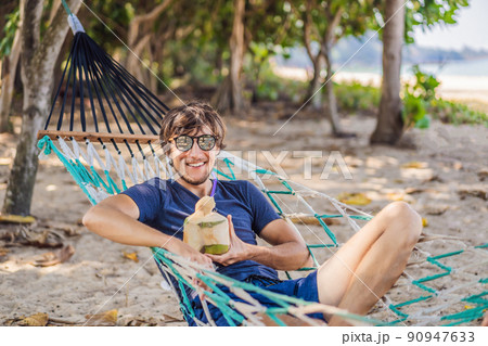 Young man on the beach in a hammock with a drink 90947633
