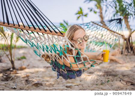 Young woman on the beach in a hammock with a drink Young woman on the beach in a hammock with a drink 90947649