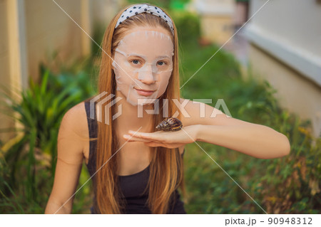 A young woman makes a face mask with snail mucus. Snail crawling on a face mask 90948312