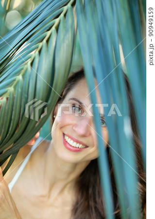 Young beautiful natural cheerful woman with healthy face and skin in exotic greenery. Closeup fresh face of attractive girl. Summer model. Natural beauty concept Young beautiful natural cheerful woman with healthy face and skin in exotic greenery. Closeup fresh face of attractive girl. Summer model. Natural beauty concept 90949159