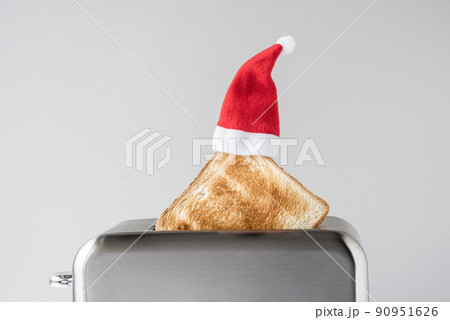 Roasted toast bread in a christmas Santa Claus red hat popping up of stainless steel retro toaster for breakfast preparation. Concept 90951626