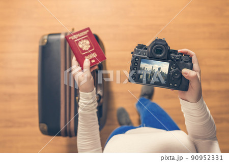 Top view on a girl looking a photos from New York city on her camera standing with suitcase in the airport. The girl returns home after trip to America. 90952331