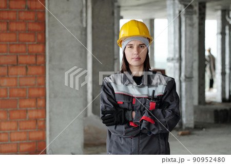 Serious female builder or engineer in workwear standing in unfinished building Serious female builder or engineer in workwear standing in unfinished building 90952480