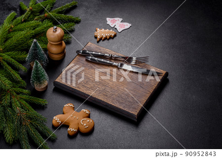 An empty wooden cutting board with wooden cutlery on a christmas kitchen table An empty wooden cutting board with wooden cutlery on a christmas kitchen table 90952843