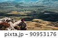 A male traveler is sitting on the edge of a cliff. A male traveler is sitting on a rock with a bird's-eye view of the valley. The concept of recreation and tourism. The man enjoys the beautiful views 90953176