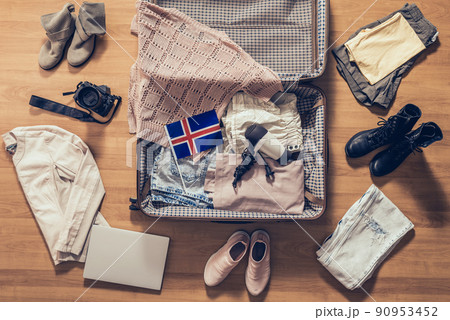 Woman's clothes, laptop, camera and flag of Iceland lying on the parquet floor near and in the open suitcase. Travel concept Woman's clothes, laptop, camera and flag of Iceland lying on the parquet floor near and in the open suitcase. Travel concept 90953452
